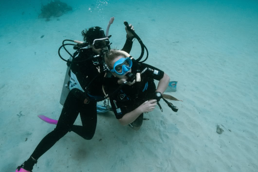 Scuba instructor guiding a student through a breathing exercise on the sandy sea floor