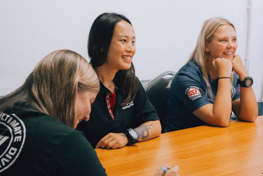 Three scuba diving professionals smiling and taking notes during a classroom training session