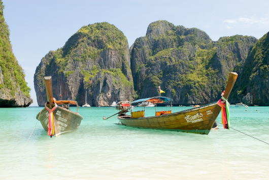 Traditional Thai longtail boats floating in clear turquoise water at Maya Bay, surrounded by limestone cliffs