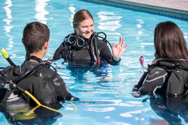 Scuba instructor smiling and giving the OK hand signal to students during a pool training session
