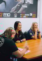 Three scuba diving professionals smiling and taking notes during a classroom training session