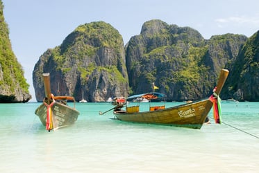 Traditional Thai longtail boats floating in clear turquoise water at Maya Bay, surrounded by limestone cliffs