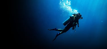 Scuba diver swimming alone in deep blue water with air bubbles rising to the surface